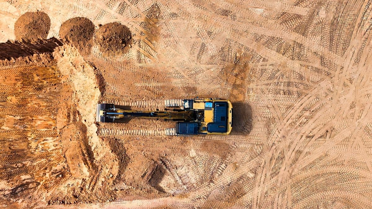 Aerial view of an excavator carving out earthworks on a large bare-soil construction site