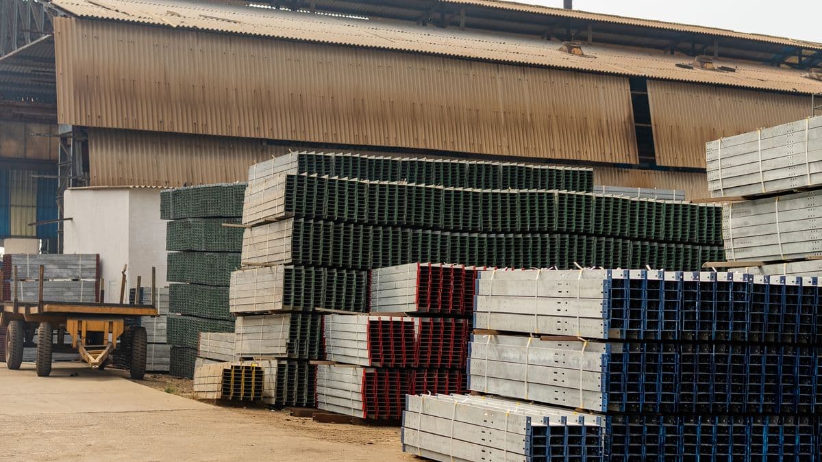 The corrugated metal exterior of an industrial warehouse with stacks of steel and metal materials stored outdoors in the yard.