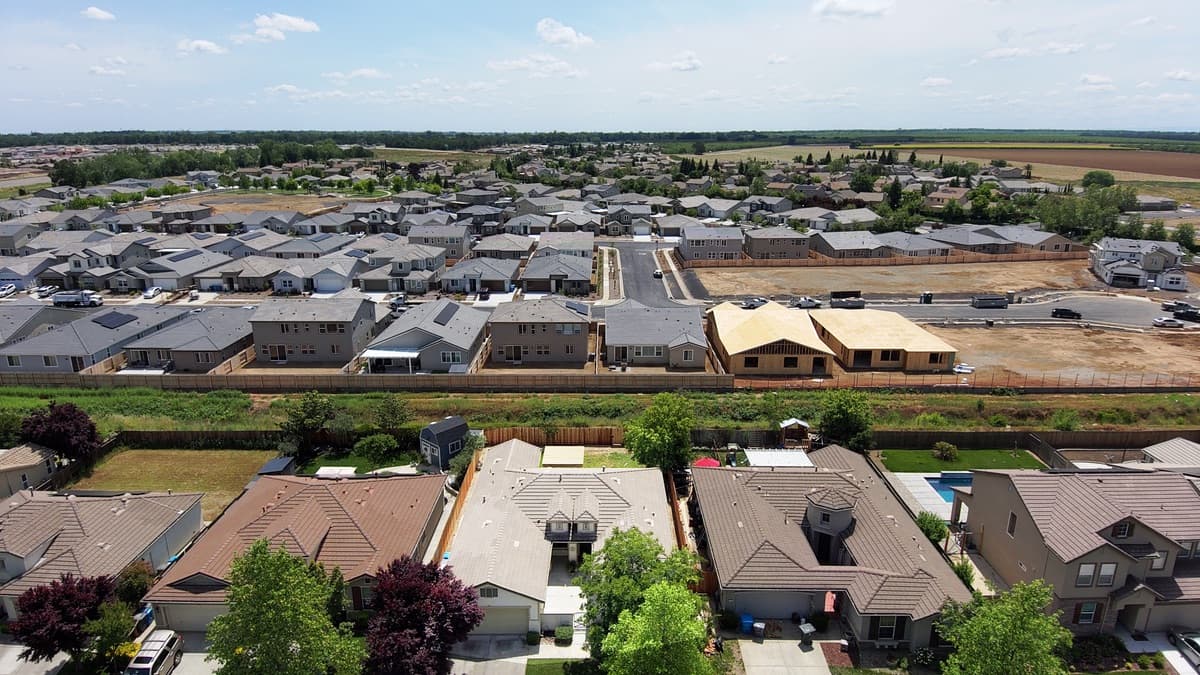 Aerial view of a residential subdivision with finished houses in the foreground and bare, graded lots still under active development stretching into the distance.