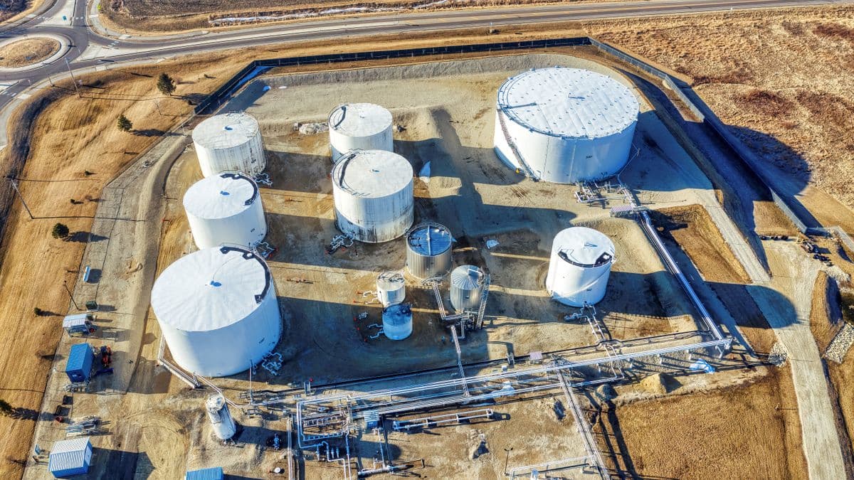 Aerial view of an aboveground oil storage tank farm with several large white tanks inside a bermed containment area beside an access road.