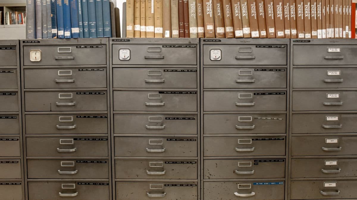 Rows of labeled metal filing cabinet drawers topped with a shelf of archived binders and reference volumes