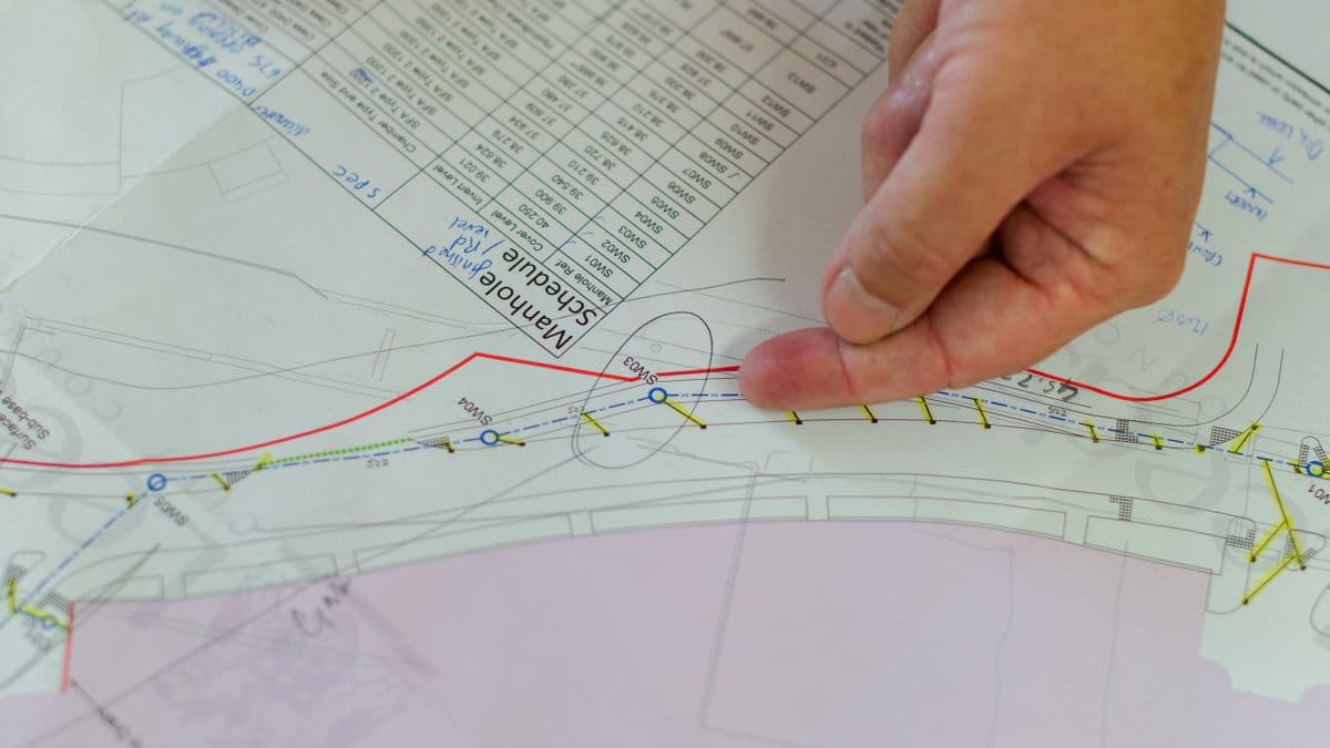 Close-up of hands reviewing a rolled-out site plan showing property boundary lines, a drainage channel and a data table.