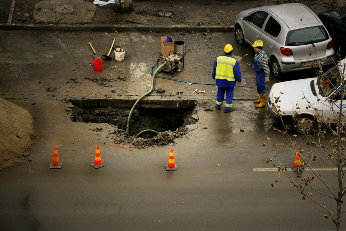 A construction crew installing drainage piping in an open trench at a job site, with silt fencing visible along the perimeter