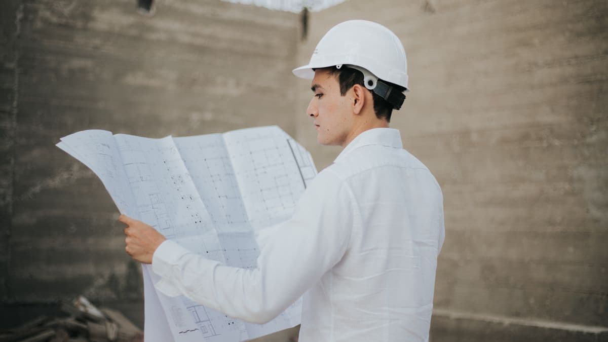 An engineer in a hard hat reading a rolled-out blueprint on a concrete construction site